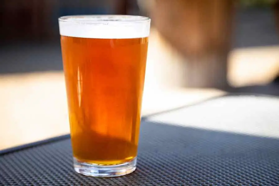 A pint glass of beer on a table in an outdoor patio bar or pub setting.