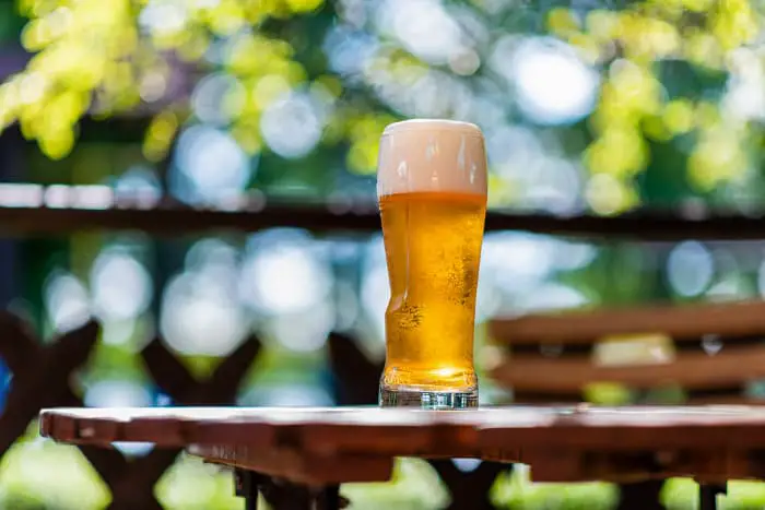 Glass of beer on table in outdoor beer garden setting.