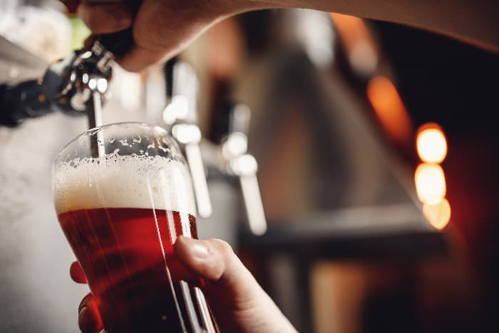 Person filling glass with amber ale or red lager beer.