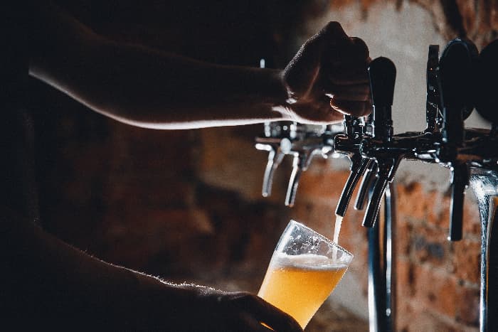 Bartender pouring light-colored beer in glass from draft tap. Vic Secret hops are used to make pale ales, IPAs, stouts, and porters.