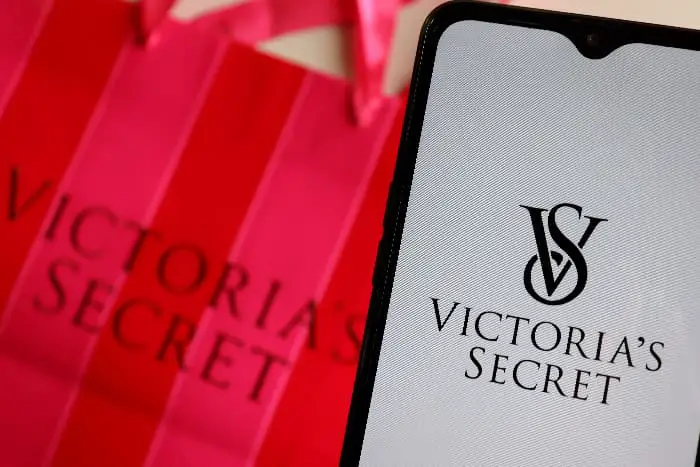 Victoria's Secret shopping bag and smartphone with Victoria's Secret logo on the screen.