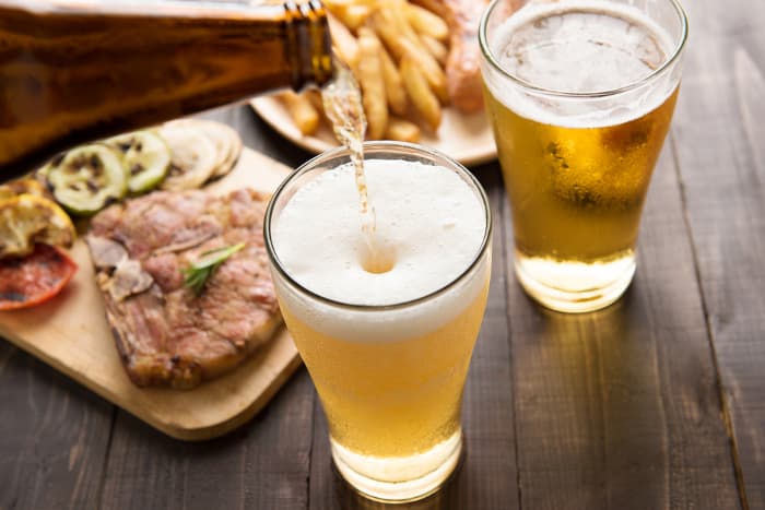 Beer being poured into a glass with food nearby.