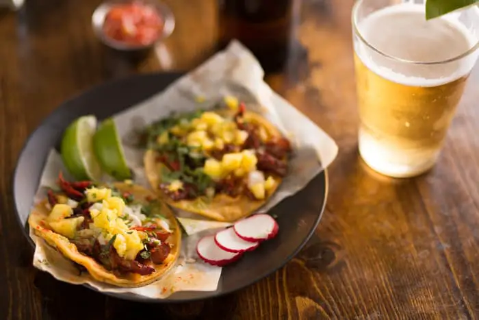 A plate of street tacos and a pint glass of pale colored beer.