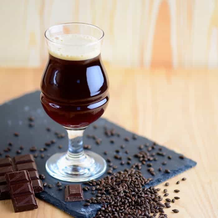 A glass of dark-colored chocolate beer with coffee beans and squares of dark chocolate.