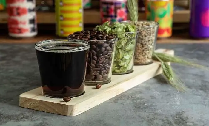 Beer flight glasses with dark beer, coffee beans, beer hops, and roasted barley or malt.  Coffee beer concept.