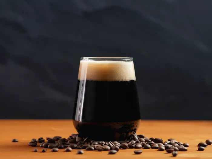 Glass of coffee beer surrounded by coffee beans.