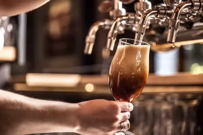 Person pouring dark draft beer into a glass.