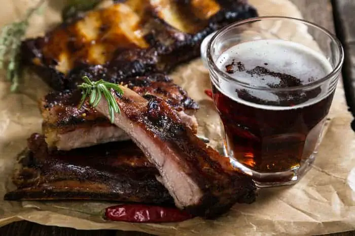A glass of dark beer next to grilled ribs.