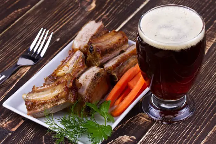 A glass of dark beer with a plate of beef ribs.