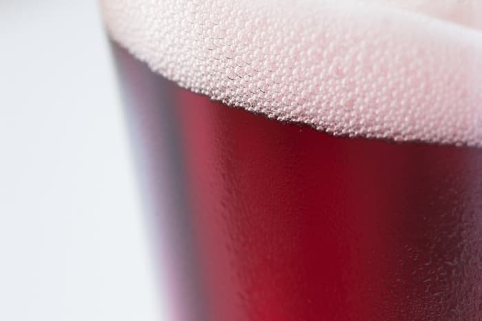 Closeup of a pint glass of red-colored fruit beer.