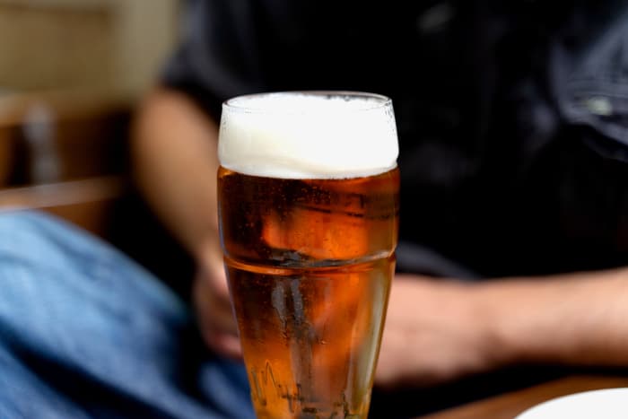 Glass of beer with man seated nearby.