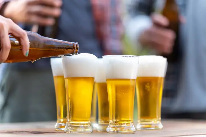 Person pouring light-colored beer into fluted beer glasses.