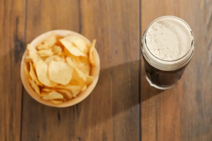 Overhead view of glass of dark beer and bowl of chips.