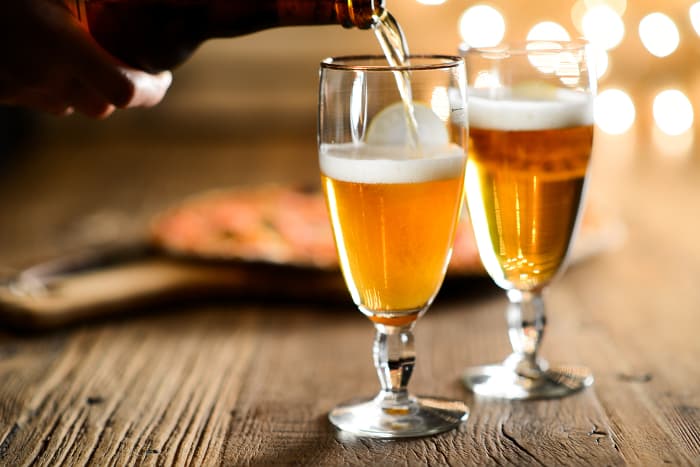 Person pouring beer into tall glasses.