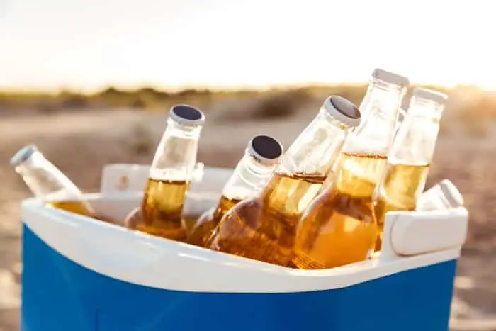 Closeup of a blue cooler with bottles of light-colored beer in a beach setting.