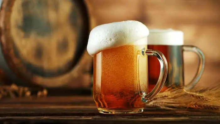 Two mugs of medium- to light-colored beer.