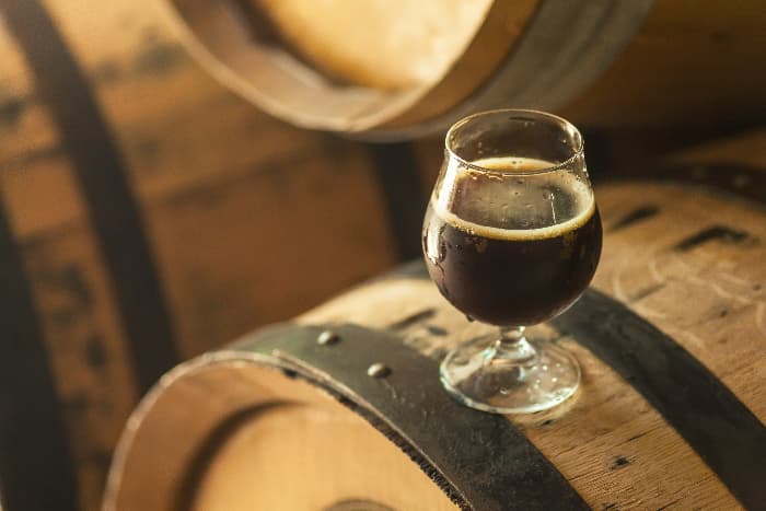 A goblet of dark beer on a barrel. Number of beer barrels produced per year determines what is micro brewery in the industry.