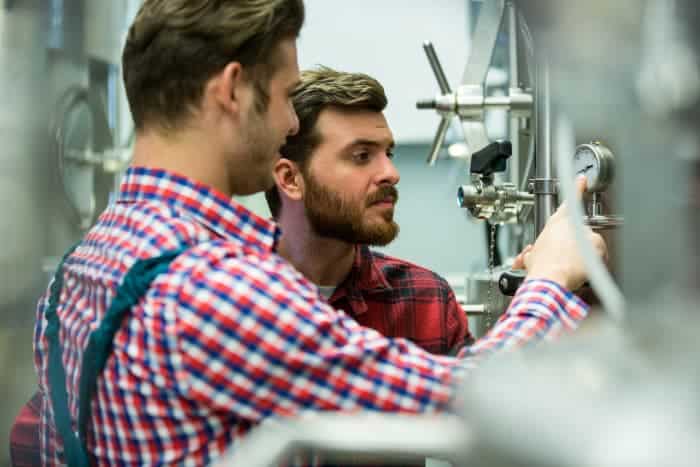 Two men looking at readings on brewery equipment.