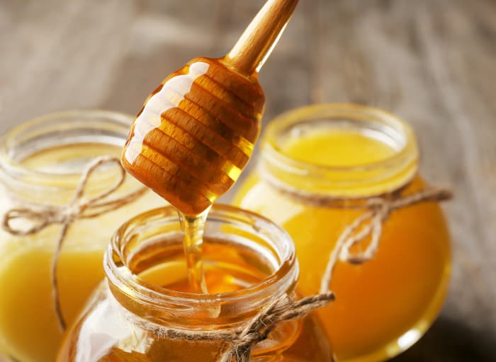 Wooden honey dipper and three jars of honey.