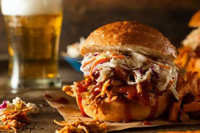 Closeup of a pulled pork sandwich with a pint of beer in the background.